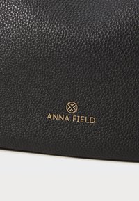 Black textured leather handbag featuring a gold embossed logo "ANNA FIELD" with a circular accent above the text.