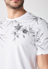 White t-shirt with black floral print on the upper half, short sleeves, and round neckline. Soft fabric with a smooth texture.
