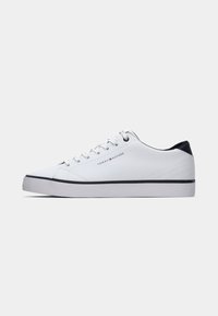 White sneaker with a smooth texture, round toe, and white laces. Navy accent on the heel, featuring a black rubber sole and minimal branding.