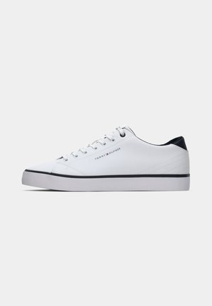 White sneaker with a smooth texture, round toe, and white laces. Navy accent on the heel, featuring a black rubber sole and minimal branding.