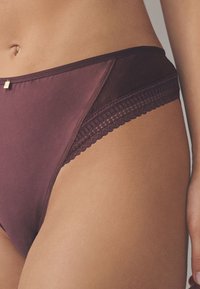 Sous-vêtements hipster bordeaux foncé en tissu lisse, avec une bordure en dentelle et un petit accent décoratif doré. Dotés d'une ceinture plate et d'un design sans coutures.