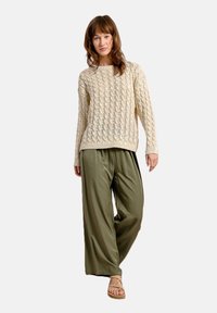Maglione a trecce color crema abbinato a pantaloni a gamba larga verde oliva, caratterizzato da una consistenza morbida e una vestibilità rilassata. Sandali semplici completano l'outfit.