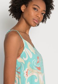 Um vestido turquesa com um padrão floral, apresentando alças finas, um decote em V e uma textura suave. O design inclui formas curvas em tons suaves.