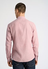 Camicia a maniche lunghe in tessuto rosa chiaro con finitura testurizzata, dotata di colletto a lavorazione a bottoni e bottoni ai polsini, abbinata a jeans in denim scuro.