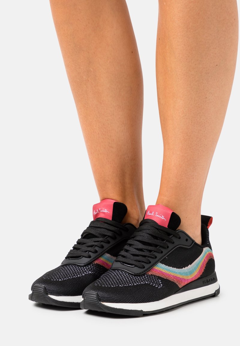 Baskets noires avec une texture tissée, dotées d'accents latéraux colorés, de lacets noirs et d'une languette de talon rose avec logo. Semelle en caoutchouc.