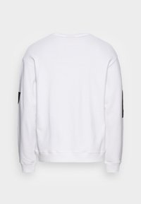 Sudadera blanca hecha de tela suave, con mangas largas, cuello redondo y un detalle negro en la manga izquierda. Vista trasera mostrada.