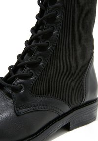 Bottine noire en cuir et tissu côtelé à lacets avec œillets ronds et petit talon empilé.