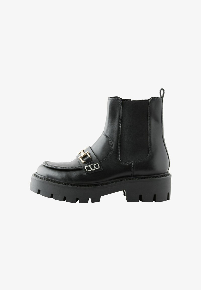 Juodas odinis kulkšninis botas su storu, tekstūruotu guminiais padu, dekoratyvine metaline sagtimi ir elastinėmis šoninėmis dalimis, kad būtų lengva užsidėti.