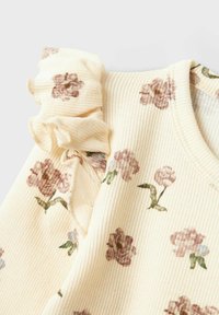 Top in tessuto giallo a coste con stampe floreali in tonalità di rosa e verde, caratterizzato da un dettaglio arricciato a volant sulla spalla.
