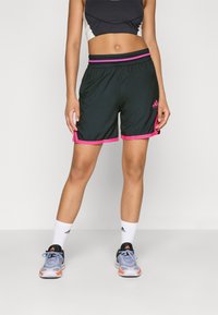Sorte atletiske shorts med pink elementer, elastisk talje, og sidesprækker, parret med grå sneakers og hvide strømper med et logo.