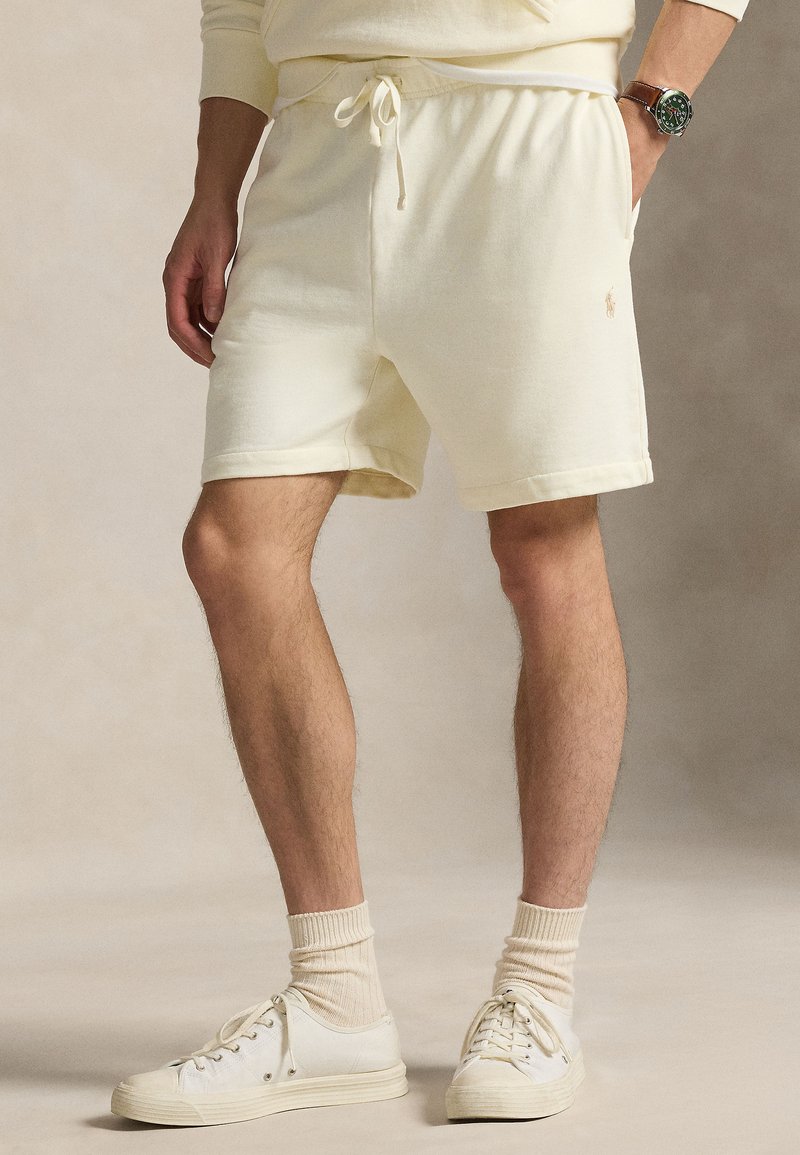 Šviesiai geltoni medvilniniai šortai su elastine juosmens juosta ir raišteliu, su šoninėmis kišenėmis ir nedideliu logotipo detaliu. Derinami su baltais sportbačiais.