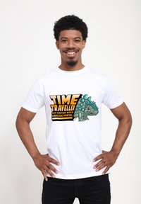 Bílý tričko s barevným grafikou dinosaura a textem: "CESTOVATEL V ČASE Z JINÉHO SVĚTA JURASSICKÝ PORTÁL" v tučných písmenech.