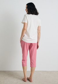Outfit casual con una t-shirt in cotone crema e pantaloni capri rosa, mostrato da dietro. I pantaloni hanno tasche e una vestibilità rilassata.