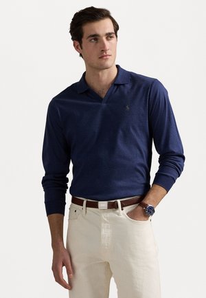 Camisa polo de manga larga en color marino con escote en forma de V, que presenta un pequeño logo en el pecho, combinada con pantalones crema claros y un cinturón de cuero marrón.