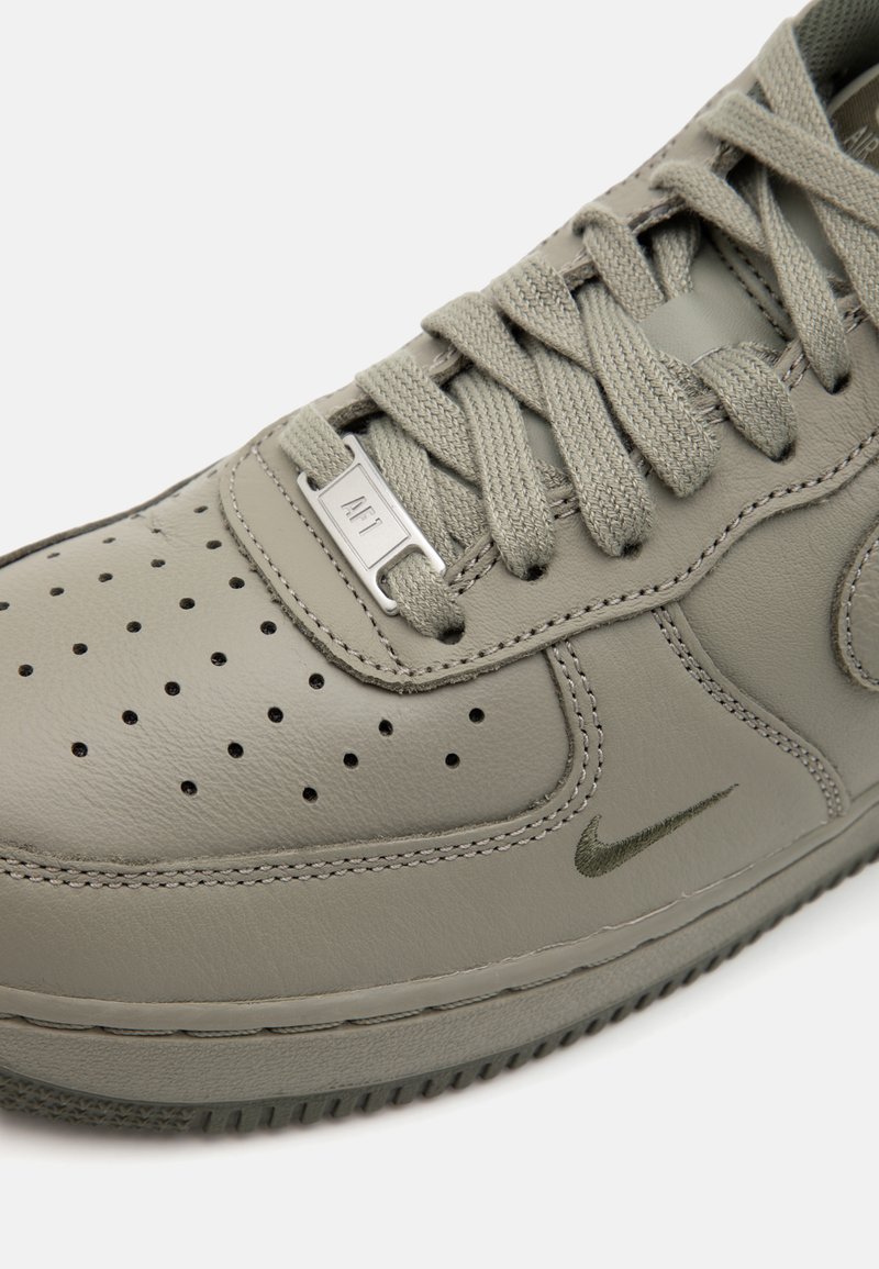 Zapatilla de cuero gris con perforaciones, cordones texturizados y un logo de Nike verde. Presenta una lengüeta acolchada y una suela de goma.