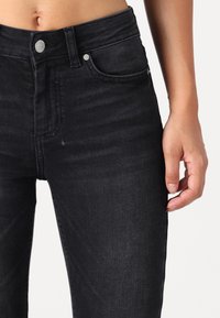 Jeans negros de cintura alta fabricados en denim, con un diseño clásico de cinco bolsillos y un ligero desvanecimiento, con una textura suave y botón plateado.