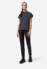 Dunkelgraues kurzärmliges T-Shirt mit lockerer Passform, kombiniert mit schwarzen Lederhosen mit strukturiertem Finish und wuchtigen schwarzen Stiefeln.