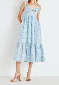 Blå mönstrad klänning med utsvängt kjoldel, justerbara snörband och en nyckelhålsutskärning. Matchad med nude blockklack-sandaler.