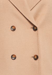 Cappotto di lana beige con ampio rever e quattro bottoni rotondi in tartaruga disposti in uno stile doppiopetto.