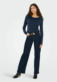 Marineblå langærmet top med draperet udskæring, parret med højtaljede mørke denimjeans og sorte hælede ankelstøvler.
