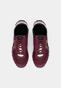 Um par de ténis Reebok cor burgundy com detalhes brancos e solas pretas, vistos de cima sobre um fundo branco liso.