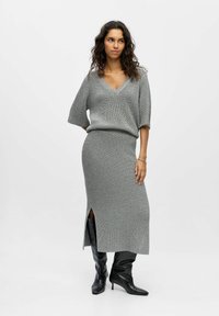 Ensemble en tricot gris composé d'un haut à manches courtes et décolleté en V et d'une jupe mi-longue avec une fente sur le côté, associé à des bottes noires montant jusqu'aux genoux.