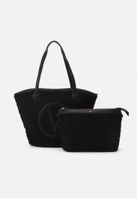 Svart strukturert totebag med en stor logo og en mindre matchende veske. Begge har syntetisk materiale og tekstur i kunstig pels.