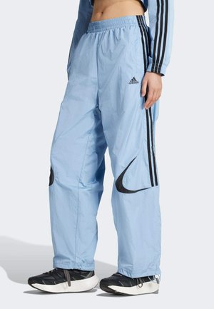 Lichtblauwe trainingsbroek met zwarte Nike- en Adidas-logo's, elastische tailleband, zijzakken en zwarte strepen langs de zijkanten.