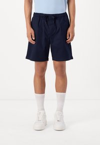 Shorts de bain bleu marine avec taille élastique et cordon de serrage. Associés à des chaussettes blanches et des baskets. Tissu lisse et coupe au genou.