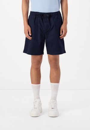 Mørkeblå svømmedragt med elastisk talje og snor. Stylet med hvide sokker og sneakers. Glat stof og knælang skæring.