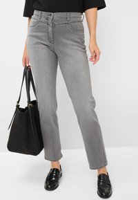 Jeans in denim grigio con taglio dritto, caratterizzati da una vita alta, passanti per cintura e cuciture sottili. Indossati con mocassini neri e una borsa nera.