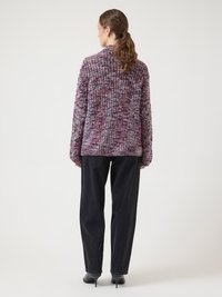 Lila und pink texturierter Strickpullover mit hohem Kragen, getragen über schwarzen, weit geschnittenen Hosen, mit langen Ärmeln und legerer Passform.