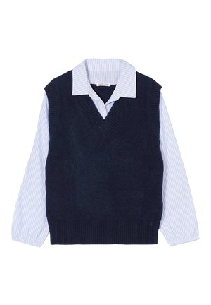 Marineblå ærmeløs sweater med V-hals, lagd oven på en hvid skjorte med blå striber. Har ribbede kanter og manchetter med knapdetaljer.