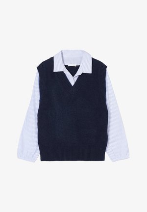 Marineblauwe mouwloze trui met V-hals, gelaagd over een wit shirt met blauwe strepen. Heeft ribbelranden en knoopdetails op de manchetten.