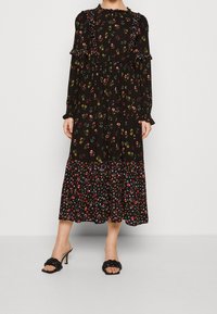 Abito nero floreale con maniche lunghe, scollo a rouches e orlo a strati. Presenta motivi floreali multicolori e una silhouette rilassata.