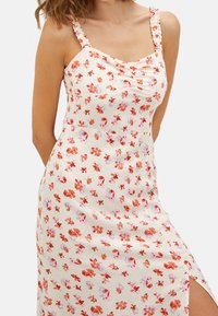 Blumenkleid mit einem cremefarbenen Hintergrund, das orangefarbene und pinke Blumen zeigt. Volantträger, taillierter Oberteil und seitlicher Schlitz.