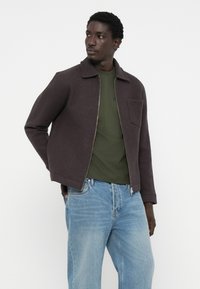 Dark gray wool-blend jacket with a collared design, featuring a chest pocket and a zipper. Paired with a green shirt and light blue jeans.