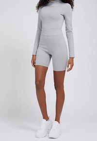 Vale vaaleanharmaa urheilumallinen bodysuit, jossa on pitkät hihat, korkea vyötärö ja tiukat shortsit; valmistettu sileästä, joustavasta materiaalista. Brändilogo rinnassa.