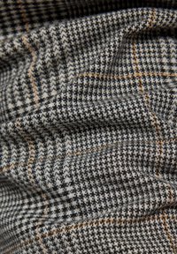 Textil mit Hahnentrittmuster in Schwarz, Grau und Weiß mit orangefarbenen Akzenten; strukturierter Stoffvorhang erzeugt Tiefe.