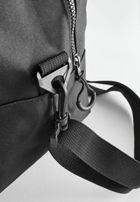 Zwarte nylon tas met een rits, verstelbare banden en metalen hardware. Textuur oppervlak met stevige clips en een geweven strap.