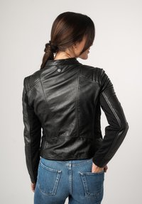 Schwarze Leder-Motorradjacke mit taillierter Passform, auffälligen Nähten und Druckknopfverschluss. Kombiniert mit blauen Denim-Jeans.