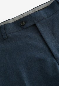 Granatowe, dopasowane spodnie o subtelnej fakturze, z plisą z przodu, pojedynczym zapięciem na czarny guzik oraz kontrastową podszewką w pasie wewnętrznym.