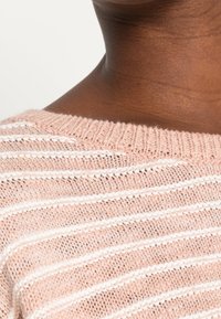 Jasnoróżowy sweter dzianinowy z białymi poziomymi paskami. Posiada szeroki dekolt i teksturowany materiał, co przejawia luźny i przewiewny fason.