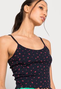 T-shirt de alças em azul-marinho, com pequenos padrões florais vermelhos, alças finas e uma bainha ondulada, feita de um tecido macio e elástico.