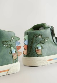 Rohelised nahast kõrgemad kingad tikitud krokodillimustriga ja värvikate soomuseaktsentidega tagaküljel. Kummist tald ja tekstuuriga pealmine osa.