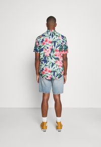 Blumiges Kurzarmhemd, navy Hintergrund, mit rosa Blumen und grünen Blättern, kombiniert mit Jeansshorts und gelben Sneakers.