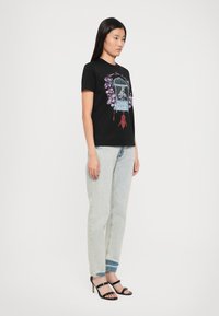 Black t-shirt with graphic print featuring a birdcage, flowers, and red accents, paired with light blue jeans and black strappy heels.