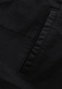Gros plan d'un tissu noir avec une ouverture de poche rectangulaire verticale cousue sur le côté droit.
