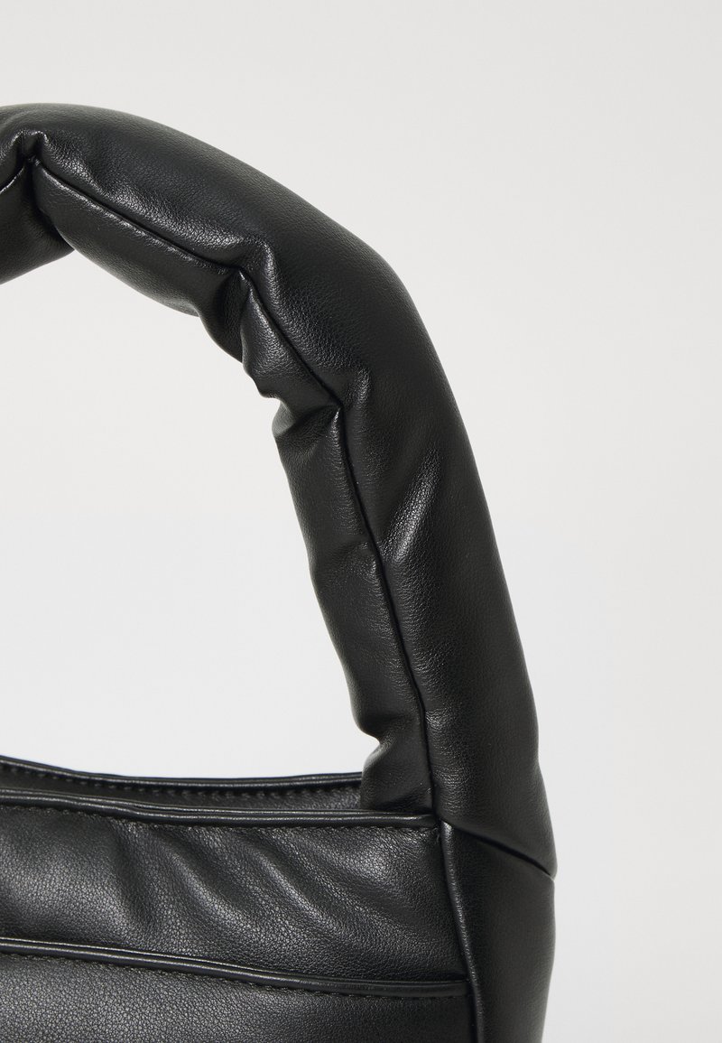 Sac en cuir noir avec une poignée rembourrée, texture lisse et forme structurée, présentant des coutures et des détails de piqûre visibles.