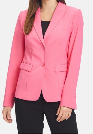 Kvinde iført en tætsiddende, knaldrød blazer med to knapper og klaplommer, kombineret med sorte bukser og en sort top under.